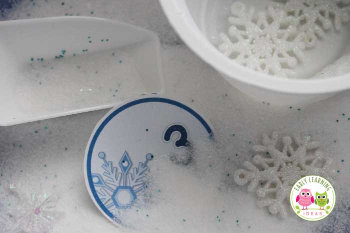 salt, glitter, number circles and containers in a winter sensory table