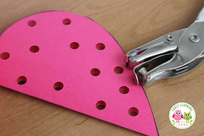 A paper heart folding half with a hole punch.  Valentine's Day Fine Motor Activities for Preschoolers