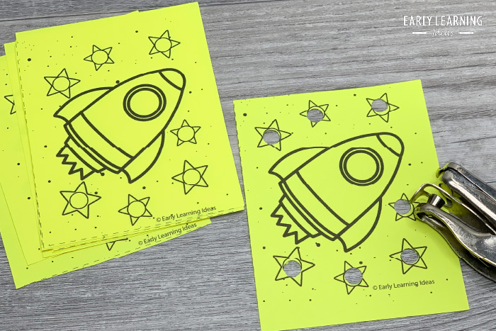 space theme fine motor printable hole punch activities.  A rocket and stars printed on bright yellow paper shown with a hole punch.