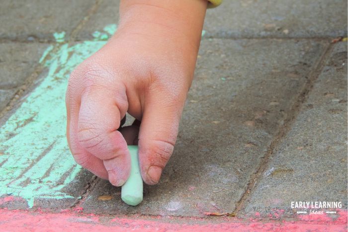 child holding a small piece of chalk to draw