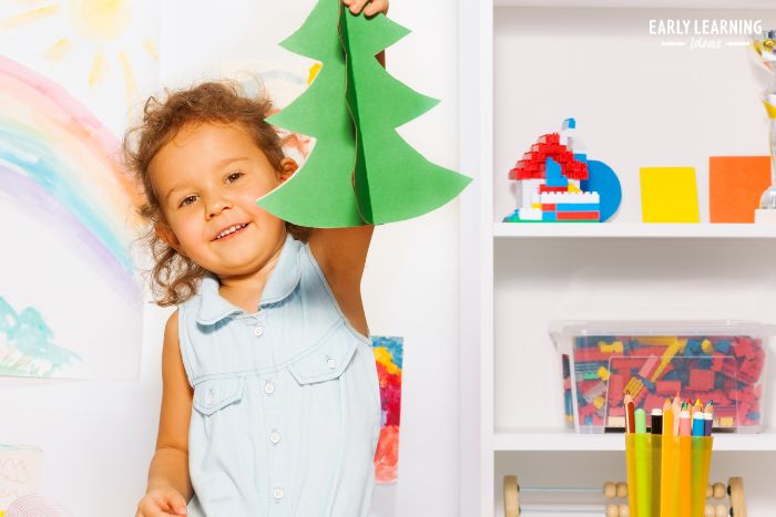 A girl proudly holding up a Christmas Tree craft as an example of how crafts help preschoolers build self esteem