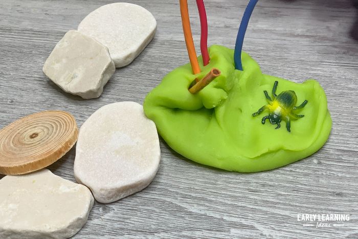 green playdough, rocks, plastic bugs, and wire are part of a fun bug playdough tray