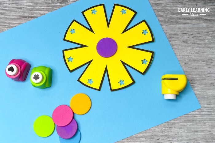 A free printable flower craft for preschoolers.  A yellow flower has been cut out and a flower hole punch is used to cut a flower shape into each petal.  The craft is a good example of how to improve cutting skills