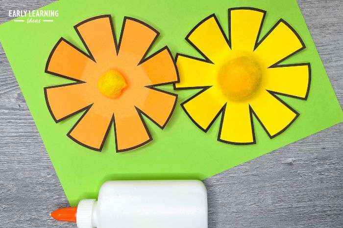 paper flower craft for preschoolers with a bottle of glue and craft pom-poms in the middle of the flowers.  The craft is an example of how to improve cutting skills.