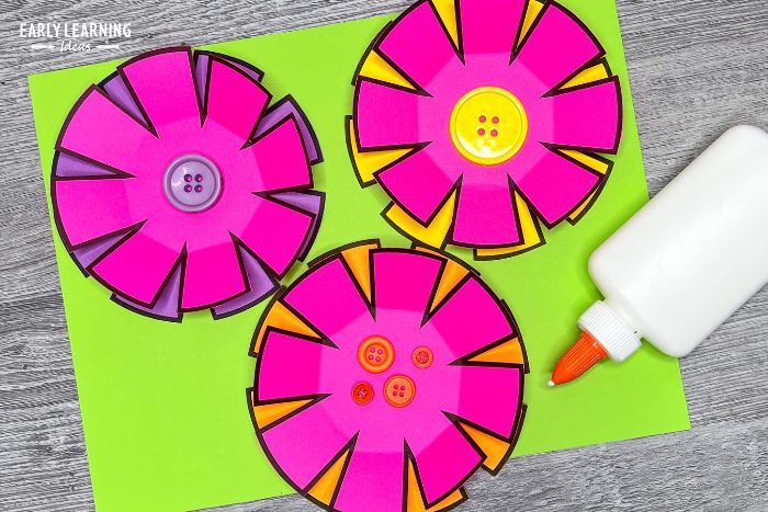 paper flower craft for preschoolers with a bottle of glue and colorful buttons in the middle of the flowers.  The craft is an example of how to improve cutting skills.