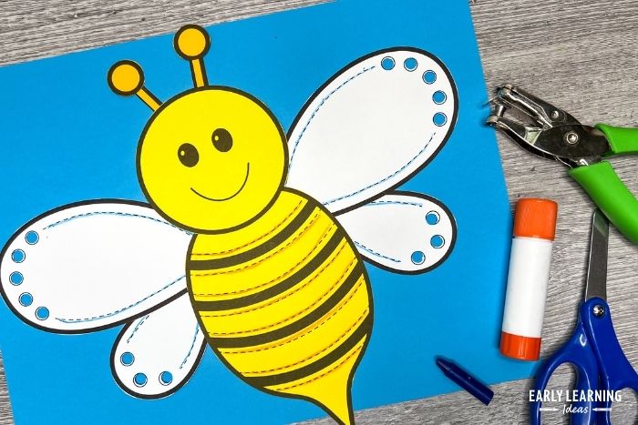 This preschool bumble bee craft is a great fine motor activity for spring.  The image includes a crayon, glue stick, scissors, and a hole punch.  There are holes in the bumble bees wings because the craft is also an example of hole punch activities.