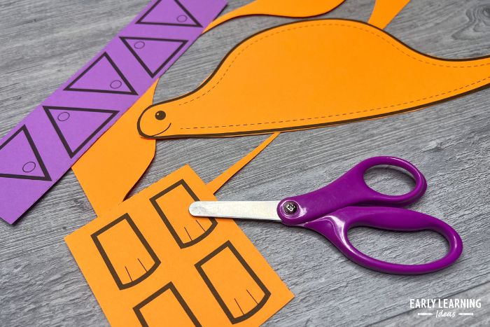 dinosaur printable fine motor crafts for kids.  An orange dinosaur with a pair of purple scissors.
