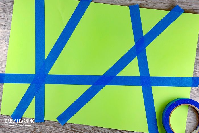 Blue masking tape on green paper to mask the paper as kids paint with spay bottles.  This is an example of easy painting activities for kids in preschool
