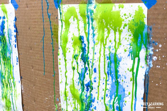 squirt gun painting - blue, green, and white paint sprayed and dripping on a piece of white paper.
