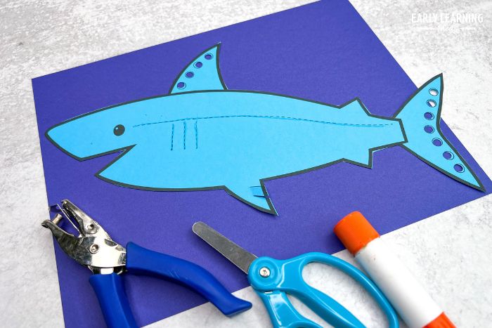 A shark craft printed on teal paper and glued to a dark blue background - an example of under the sea crafts for preschoolers
