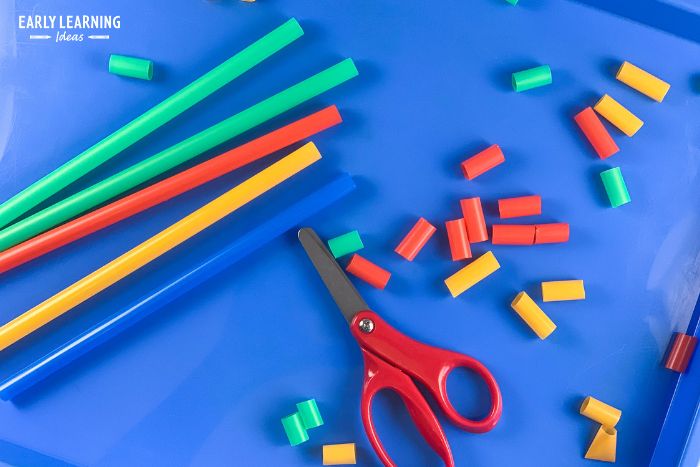 colorful plastic straws from the Dollar tree and a pair of scissors on a blue tray..  A child has cut up some of the straws into small pieces to use for dollar store preschool activities.