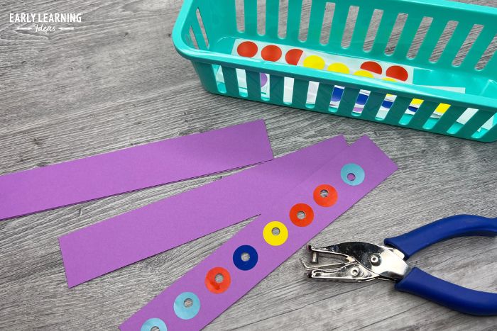 Dot stickers on a strip of purple paper with a hole puncher.  A child has punched holes in each of the dots.  An example of dot sticker activities for fine motor skills.