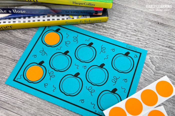 Pumpkin fine motor task cards with a orange dot stickers and pile of children's books
