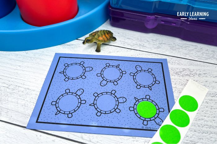 A turtle themed fine motor task cards shown with green dot stickers and a small plastic turtle - an example of a fun and simple scavenger  hunt activity for preschoolers.