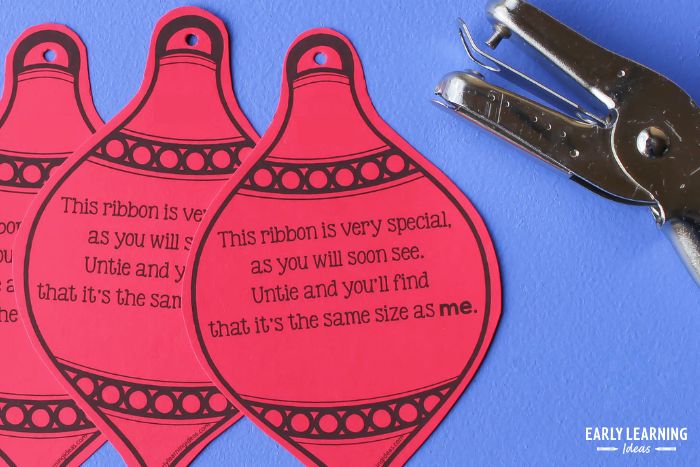 printable ornaments with ribbon as a preschool gift for parents.  Three printable ornaments printed on red paper shown with a hole punch.