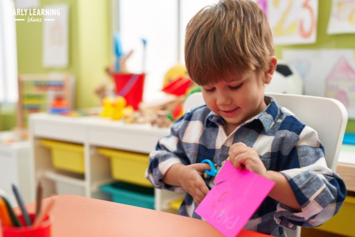 A child in preschool classroom cutting a piece of pink paper