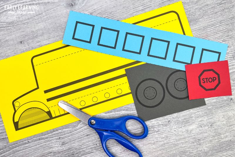 printable school bus craft template printed on yellow, blue, black and red paper and shown with scissors.
