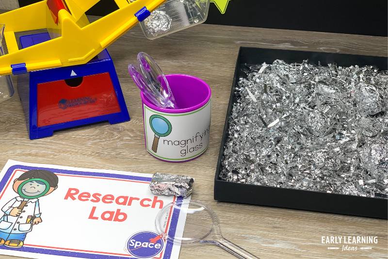 A balance scale, magnifying glass, and pretend space rocks in a space dramatic play center