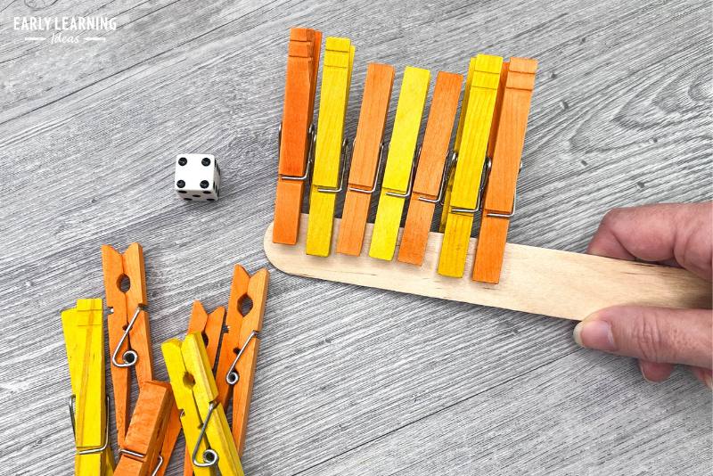 Clothespin clips on a large wooden craft stick with dice - an example of fine motor games