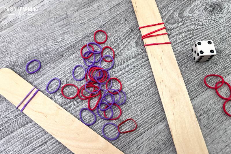 rubber band hair ties on popsicle craft sticks with dice - an example of a fine motor game for kids