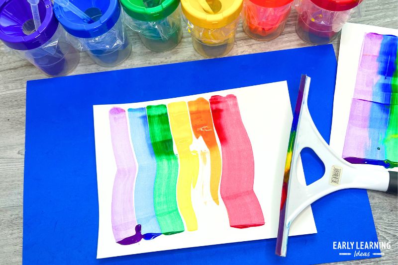 Rainbow painting activity shown with paint, eyedroppers, and a squeegee.