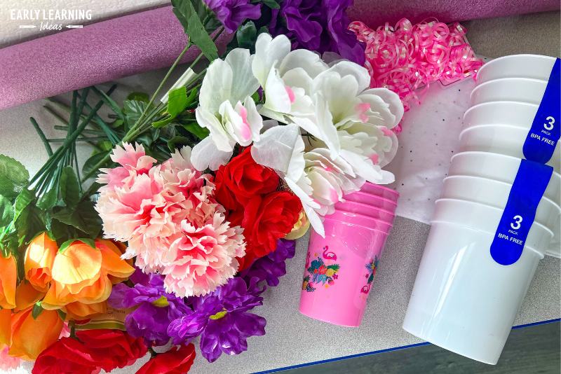 supplies for a flower shop dramatic play area that were purchased from the dollar store. Photo includes silk flowers, a pool noodle, tissue paper, gift bows, and plastic cups.