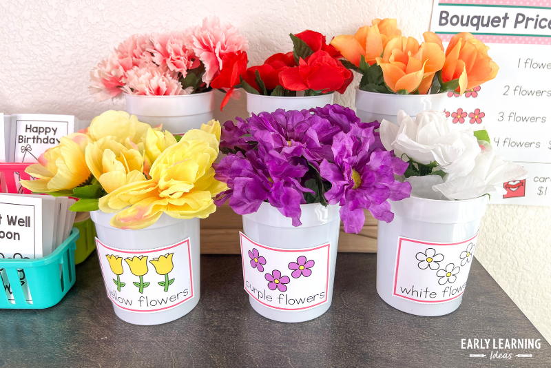 Silk flowers in plastic cups with labels in a flower shop dramatic play area.