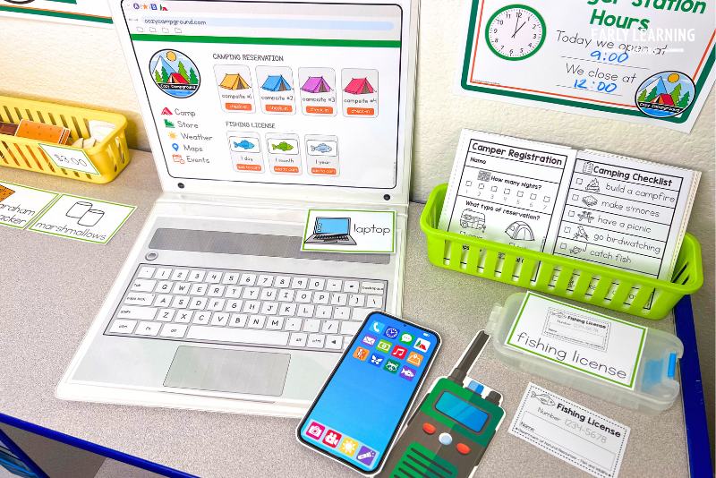 Printable camping dramatic play setup with a laptop, cellphone, walkie talkie, and fishing license