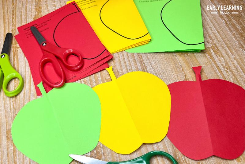 An apple cutting activity. The apple cutouts were printed on red, yellow, and green paper and are shown with scissors