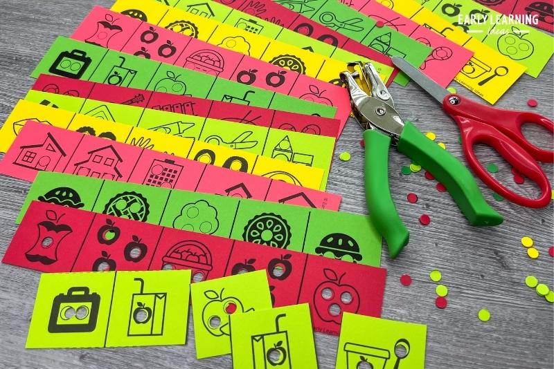 apple theme hole punch and cut strips printed on red, green, and yellow paper shown with a scissors and hole punch.