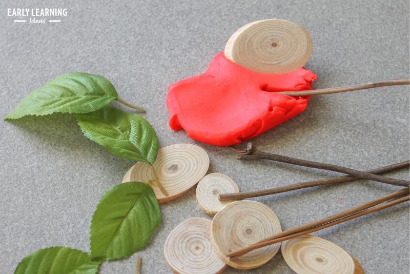 red playdough with silk leaves, wood pucks, and sticks from an apple playdough tray
