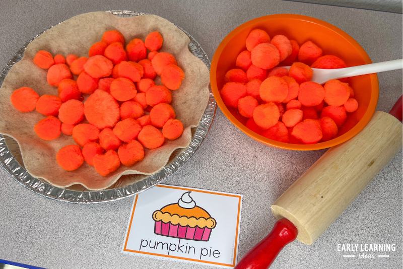 a pretend pumpkin pie made of felt and orange pom poms shown with a bowl and rolling pin.