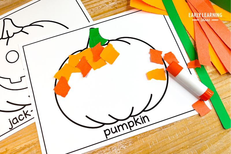 pumpkin paper tearing craft shown with a glue stick and strips of orange and green paper