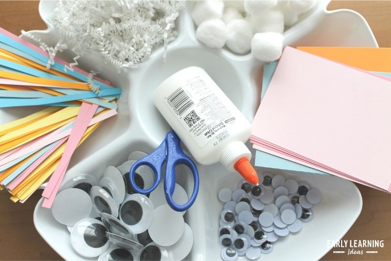 A divided container with supplies for an Easter bunny craft project. The container has glue, googly eyes, strips of paper, cotton balls, and white paper shred in it.