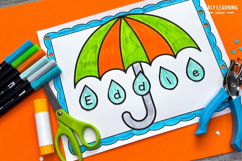 no-prep umbrella name craft and fine motor activity is shown with a hole punch, markers, scissors, and a glue stick for April showers theme