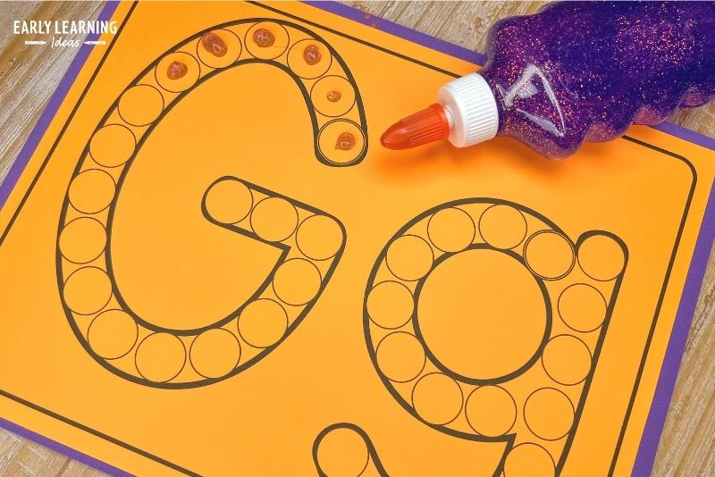 A letter g dot letter printable is shown with a bottle of purple glitter glue. A dot of glue has been applied to the dots that make up the letter G