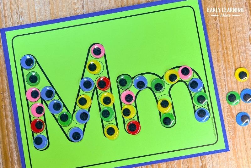 A letter m dot letter printable is shown with colorful googly eyes on each of the dots