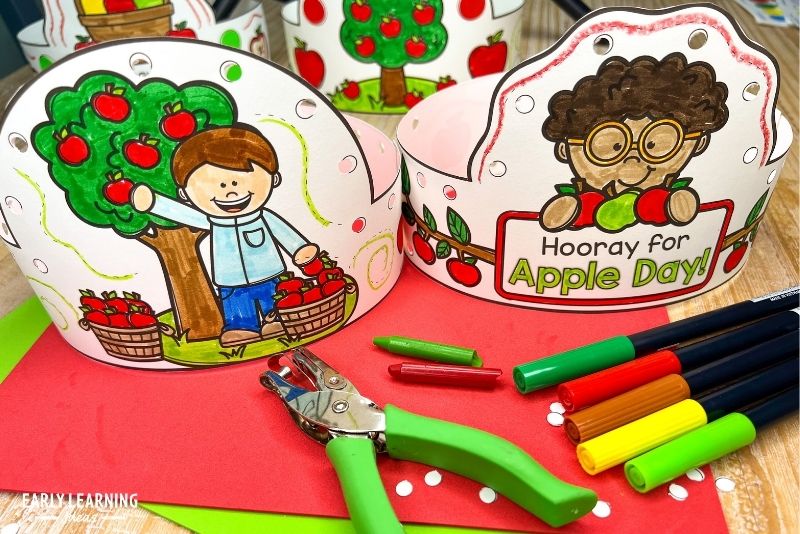 apple headband crown craft for kids. - an example of an apple fine motor activity. Shown with markers, crayons, and a hole punch.